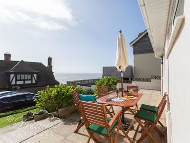 A patio with wooden table and chairs with an umbrella overlooking the sea at Seacliff in West Bay