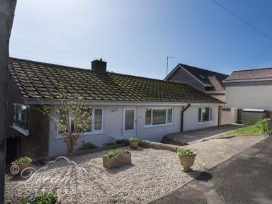 A small house with a tiled roof gravel garden with flower pots and a concrete driveway at Seacliff in West Bay