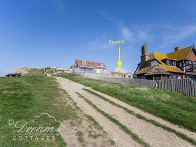 A dirt path leading up to houses with a wooden fence under a blue sky at Seacliff in West Bay