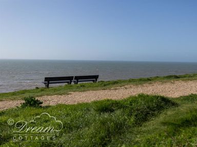 Two benches on grass next to a gravel path overlooking the sea at Seacliff in West Bay