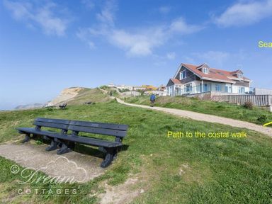 Benches on a grassy area near a path leading to a coastal walk beside a house with a red roof at Seacliff in West Bay