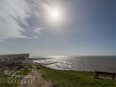 A coastal pathway leading to a beach with a bench on the grass overlooking the sea at Seacliff in West Bay