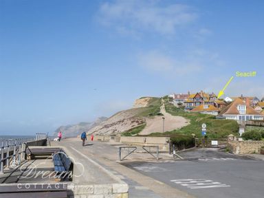 A coastal walkway with benches and people near houses on a hill at Seacliff in West Bay