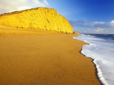 A sandy beach with waves washing ashore next to yellow cliffs under a blue sky at Seacliff in West Bay