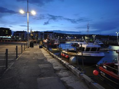 A dockside with boats moored in the water and streetlights illuminating the area at Seacliff in West Bay