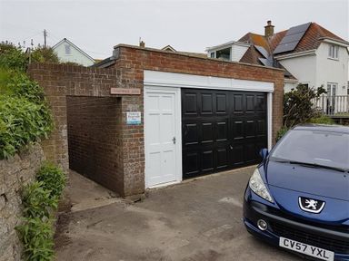 A driveway with a blue car parked next to a brick garage with a white door and black garage door at Seacliff in West Bay
