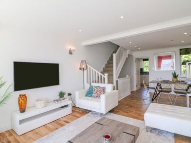 A living room with a mounted TV white chair and dining table near stairs at Sea King House in Cove Castle