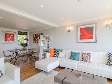 A living room with a white sectional sofa with colorful cushions a wooden coffee table a dining table with chairs and wall art at Sea King House in Cove Castle