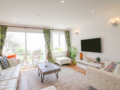 A living room with white sofas green curtains a wooden coffee table and a TV on the wall at Sea King House in Cove Castle