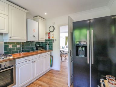 A kitchen with white cabinets wooden countertop green tiled backsplash black refrigerator and an open door to a dining area at Sea King House in Cove Castle