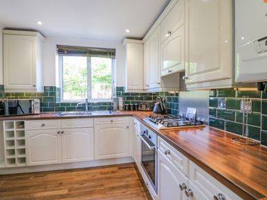 A kitchen with white cabinets wooden countertops and a window above the sink at Sea King House in Cove Castle