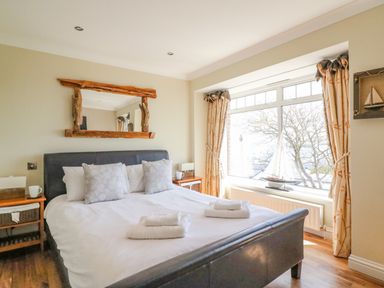 A bedroom with a large bed white linens and pillows a wooden floor a window with curtains and a sailboat model at Sea King House in Cove Castle