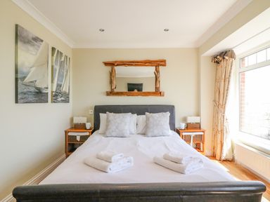 A bedroom with a bed pillows folded towels bedside tables with lamps and cups a wooden mirror and window at Sea King House in Cove Castle