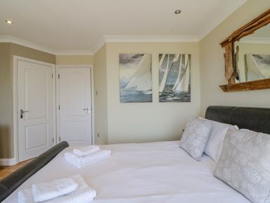 A bedroom with a made bed and towels on it two doors two paintings of sailboats and a wooden framed mirror at Sea King House in Cove Castle