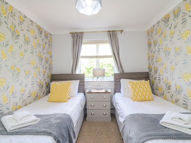A bedroom with two single beds separated by a nightstand a window with curtains and floral wallpaper at Sea King House in Cove Castle