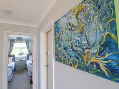 A hallway with an abstract painting on the wall and a bedroom with two single beds visible at Sea King House in Cove Castle