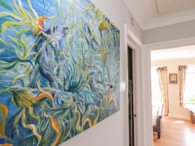 A hallway with a large painting of underwater scene with sea otters near a doorway leading to a bedroom with curtains and a framed picture at Sea King House in Cove Castle
