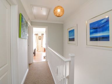 A hallway with white walls and carpeted floor with framed artwork on the walls and a light fixture on the ceiling at Sea King House in Cove Castle