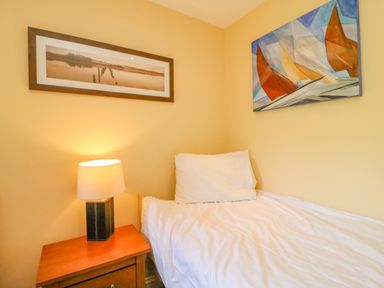 A small bedroom with a bed a pillow a nightstand with a lamp and two framed artworks on the walls at Sea King House in Cove Castle