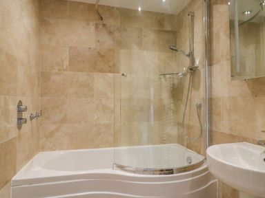 A bathroom with a bathtub shower combination and a white sink at Sea King House in Cove Castle