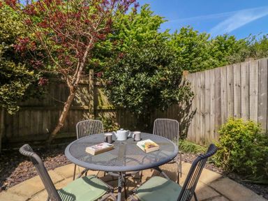 A garden patio with a metal round table and four chairs with cushions and books and a teapot on the table at Sea King House in Cove Castle