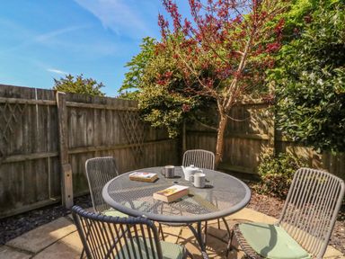 A garden patio with a round metal table and four chairs surrounded by wooden fencing and greenery at Sea King House in Cove Castle