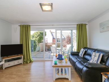 A living room with a black leather sofa and green curtains overlooking a patio at Sea Pebbles in Weymouth