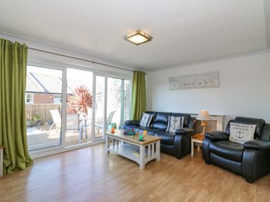 A living room with black leather sofas and a coffee table next to sliding glass doors at Sea Pebbles in Weymouth