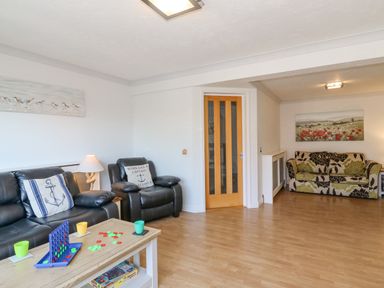 A living room with black leather sofas and a wooden coffee table with a game set at Sea Pebbles in Weymouth