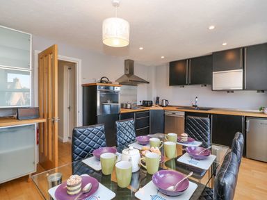 A kitchen with a glass dining table set with purple bowls and green mugs at Sea Pebbles in Weymouth
