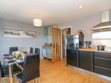 A kitchen with black dining chairs around a glass table and black cabinets at Sea Pebbles in Weymouth