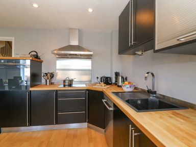A kitchen with black cabinets wooden countertops a sink a stove an oven a kettle a toaster and a bowl of fruit at Sea Pebbles in Weymouth