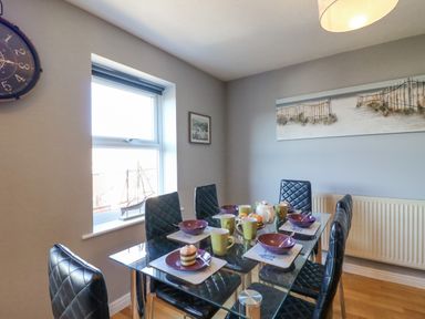A dining room with a glass table and six black chairs with plates cups and cupcakes at Sea Pebbles in Weymouth