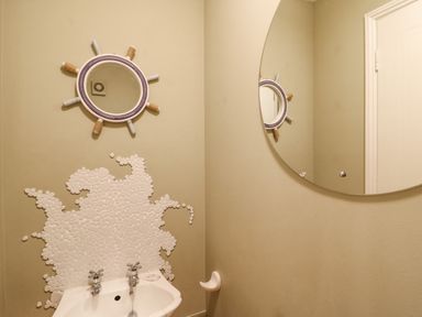 A bathroom corner with a white sink and two taps a round mirror above the sink and a circular decorative mirror on the wall at Sea Pebbles in Weymouth