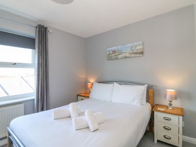 A bedroom with a double bed with white linens and towels on it with two bedside tables and lamps at Sea Pebbles in Weymouth