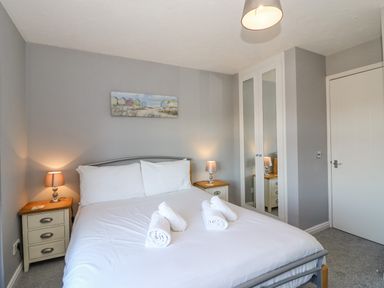 A bedroom with a double bed white linens rolled towels bedside tables with lamps and a mirrored wardrobe at Sea Pebbles in Weymouth