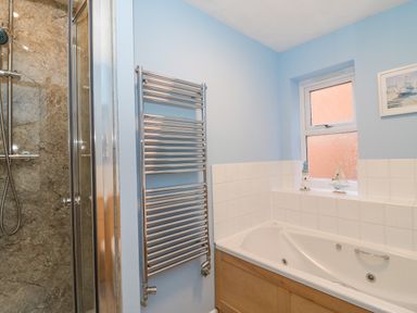 A bathroom with a bathtub wooden panel and a shower area with a glass door and chrome heated towel rail at Sea Pebbles in Weymouth