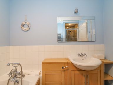 A bathroom with a bathtub sink wooden cabinet and a mirror at Sea Pebbles in Weymouth