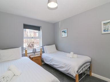 A bedroom with two single beds a nightstand with a lamp and a window at Sea Pebbles in Weymouth