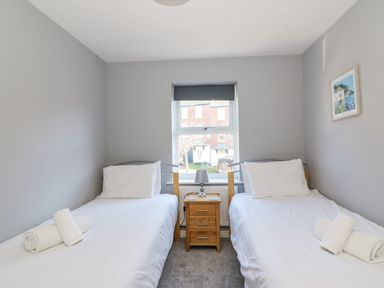 A bedroom with two single beds a nightstand with a lamp and a window at Sea Pebbles in Weymouth