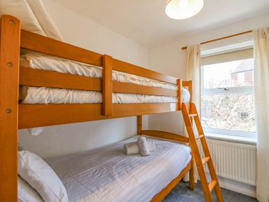 A bedroom with wooden bunk beds and a window with curtains at Sea Pebbles in Weymouth