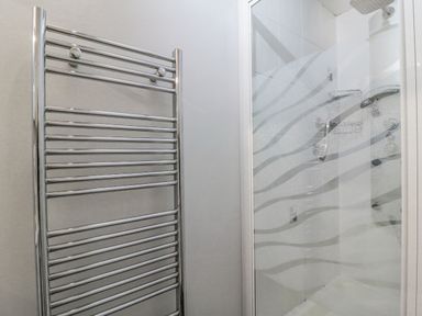A bathroom with a chrome towel radiator and a glass shower enclosure at Sea Pebbles in Weymouth