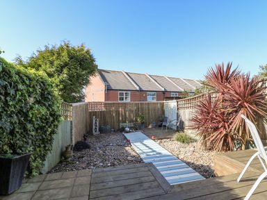 A backyard garden with wooden deck, gravel area, chairs, plants, and a wooden fence at Sea Pebbles in Weymouth