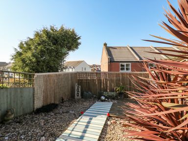 A small garden with a pebble ground and wooden pathway next to a wooden fence and a house at Sea Pebbles in Weymouth