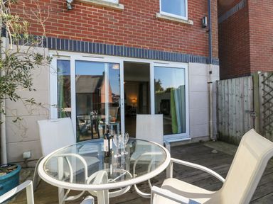 An outdoor patio area with a glass table and four chairs in front of sliding glass doors at Sea Pebbles Weymouth