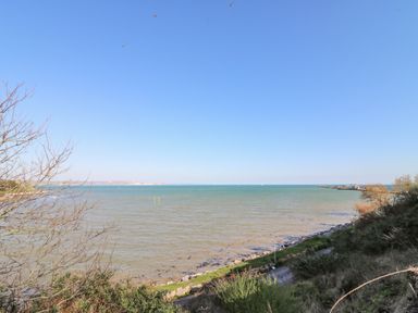 A coastal view with a blue sky and sea with a pathway and vegetation along the shore at Sea Pebbles in Weymouth