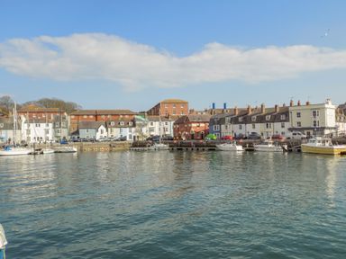 A harbor with boats docked in front of a row of houses and buildings at Sea Pebbles in Weymouth