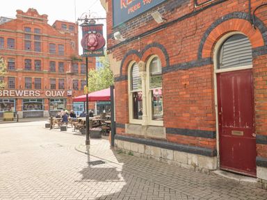 An outdoor seating area in front of a brick building with a red door and a hanging red lion sign on the street at Brewers Quay