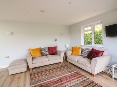 A living room with two beige sofas and colorful cushions a striped rug and a wall-mounted TV at Shipton Hill View in Shipton Gorge
