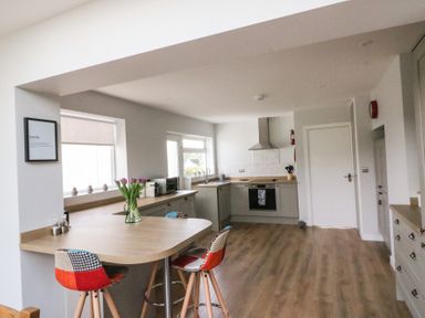 A kitchen with wooden countertops and flooring a corner oven with a hood and colorful chairs at Shipton Hill View in Shipton Gorge